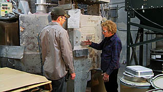 A man in a baseball cap speaking to a woman in a blue jumpsuit about combustible dust