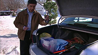 A man hovers over the open trunk of a car showing items necessary to be safe winter driving