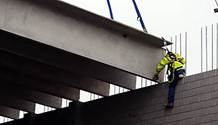 A constructionworker wearing a green vest practices fall protection on the job