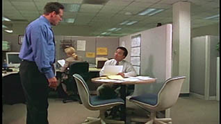 A man sitting at a desk explains to a man standing near him how to best manage expectations