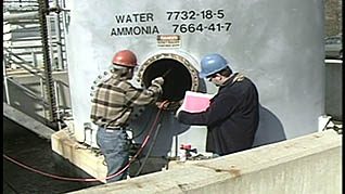 Two men in hard hats looking into a confined space