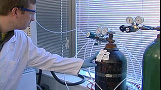 A man inspecting the tags on a gas cylinder in a laboratory
