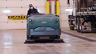 A man riding an industrial cleaning vacuum cleaning up combustible dust