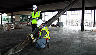 Two constuction workers wearing green vests discuss fall prevention