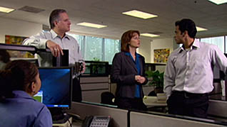 A woman stands between two men and delegates tasks to them