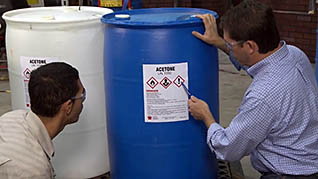 Two employees read the label on a barrel of hazardous materials