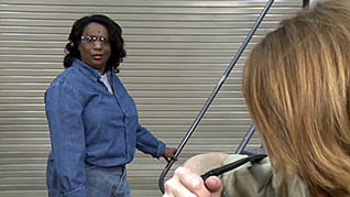 A woman in a blue jumpsuit is harassed by a coworker in an industrial setting