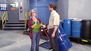 A woman wearing safety glasses and a flannel shirt talking to a man delivering a blue industrial tank discussing creating a positive workplace in indu