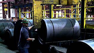 Man operating an industrial crane to move barrels