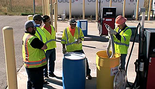 A group of workers in green vests disucss how to properly dispose of liquids in accordance with SPCC