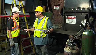 Two men in bright yellow safety vests and safety goggles discuss an accident investigation case study